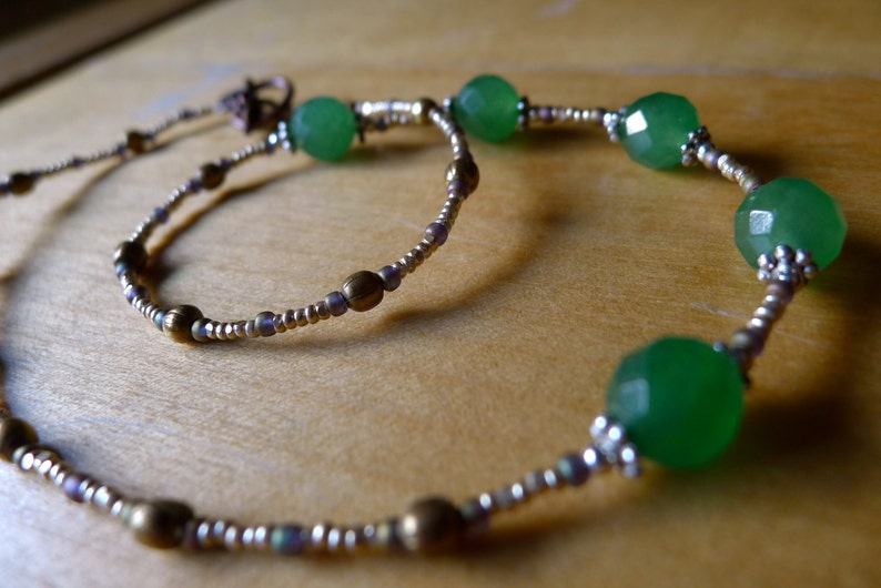 May include: A necklace with faceted green beads and smaller silver and bronze-toned beads. The beads are strung on a thin wire, creating a flowing design. The necklace has a delicate appearance. The beads have a subtle sparkle, adding a touch of elegance.