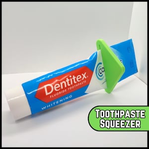 May include: A green plastic toothpaste squeezer attached to a blue and white tube of Dentex Whitening Fluoride Toothpaste.