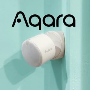 May include: A white Aqara smart home device mounted on a wall. The device has a rounded shape with a flat top and the Aqara logo is visible. The background is a light teal colour.