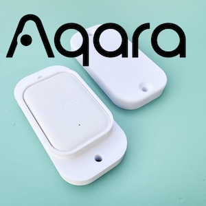 Peut inclure: Deux capteurs intelligents Aqara rectangulaires blancs avec des coins arrondis et des trous de montage à chaque extrémité. Les appareils présentent une finition en plastique lisse, une unité de capteur centrale et la marque Aqara en noir.
