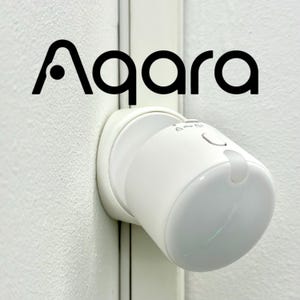 Op de afbeelding: Een witte Aqara smart home-apparaat is op een witte muur gemonteerd. Het apparaat heeft een cilindrische behuizing met een afgeronde kop en een kleine knop. Het Aqara-logo staat in zwart boven het apparaat.