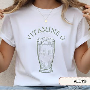 May include: White t-shirt with a green graphic of a tall glass of a frothy beverage, and the words "VITAMINE G" above it. The word "WHITE" is printed in a white box at the bottom of the shirt.