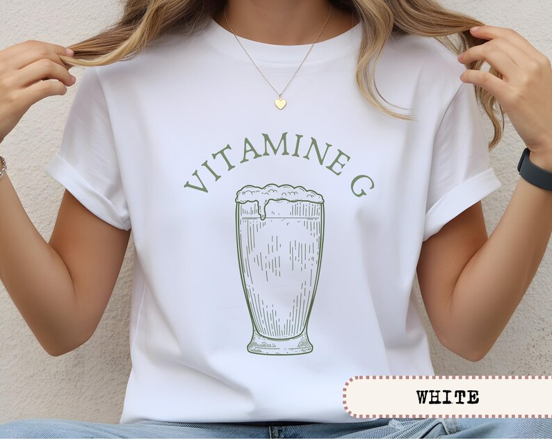 May include: White t-shirt with a green graphic of a tall glass of a frothy beverage, and the words "VITAMINE G" above it. The word "WHITE" is printed in a white box at the bottom of the shirt.