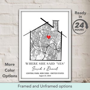 May include: A framed black and white map print in the shape of a house, with a red heart marking a location. The text reads "WHERE SHE SAID 'YES'" and includes names and a date. Additional text indicates "More Color Options" and "Framed and Unframed options."