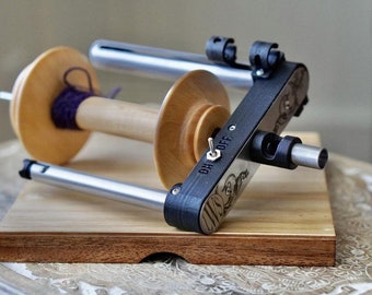 May include: A wooden spinning wheel with a black metal frame and a purple yarn on the bobbin. The wheel has a switch labeled "ON-OFF".