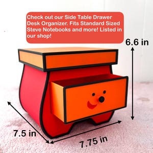 May include: A red and orange side table drawer desk organizer with a smiling face on the drawer. The organizer is 7.75 inches wide, 7.5 inches deep, and 6.6 inches tall. The text on the image says "Check out our Side Table Drawer Desk Organizer."