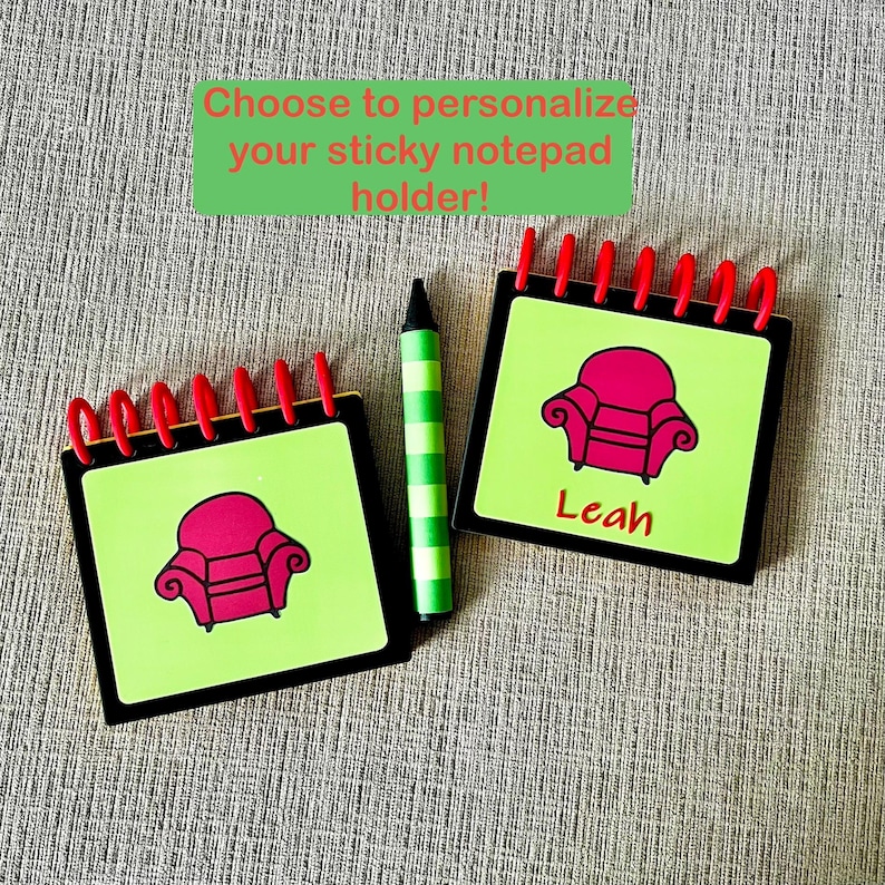 May include: Two personalized sticky notepad holders with red spiral binding, black borders, and lime green pages. Each notepad features a pink armchair graphic and the name "Leah" on one. A green and white striped crayon is also present. Text reads: "Choose to personalize your sticky notepad holder!"