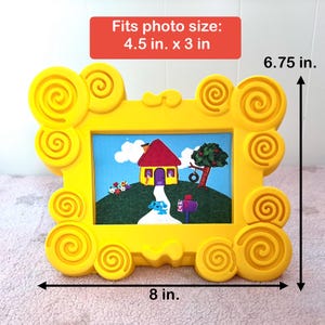 May include: Yellow picture frame with a cartoon design. The frame is 8 inches wide and 6.75 inches tall, designed to hold a 4.5 in. x 3 in. photo. The frame features a picture of a house, tree, and a blue dog.