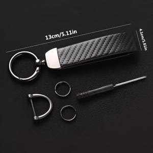 May include: A black carbon fiber keychain with a silver metal ring and accents. The keychain measures 5.11 inches long and 1.61 inches wide. Includes a screwdriver, two small rings, and a D-shaped ring.