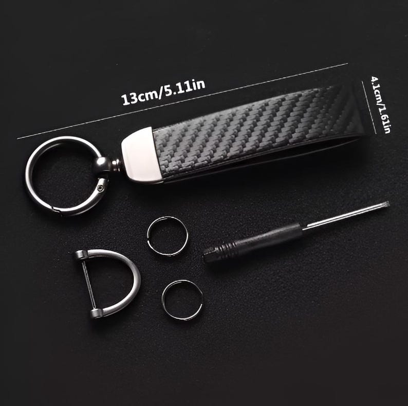May include: A black carbon fiber keychain with a silver metal ring and accents. The keychain measures 5.11 inches long and 1.61 inches wide. Includes a screwdriver, two small rings, and a D-shaped ring.