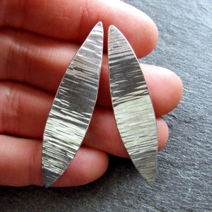 May include: A pair of silver earrings with a textured, hammered finish. The earrings are shaped like long, narrow ovals.