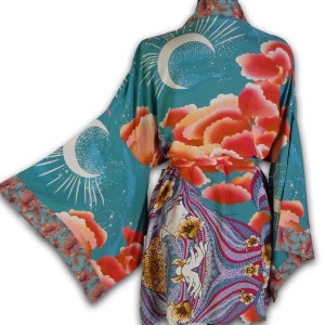 May include: A teal blue silk robe with a colorful floral and celestial print. The robe features a crescent moon, stars, and clouds. The robe is tied at the waist with a matching sash.