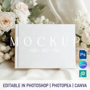Könnte beinhalten: Ein weißes Buch-Mockup mit dem Wort „MOCKUP“ in großen, eleganten Buchstaben. Der Text „PSD + JPG + PNG“ steht darunter. Das Bild ist von weißen Blumen und einem weichen, weißen Stoff umgeben. Symbole für Photoshop, Canva und Photopea sind enthalten.