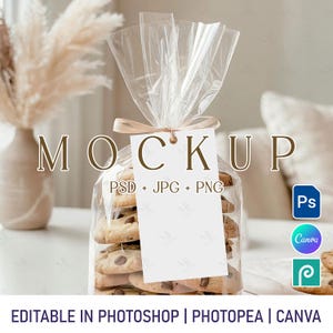 May include: A clear cellophane bag filled with chocolate chip cookies, tied with a ribbon and a blank tag. The word "MOCKUP" is displayed above the bag. The image also includes the text "PSD + JPG + PNG" and icons for Photoshop, Canva, and Photopea.