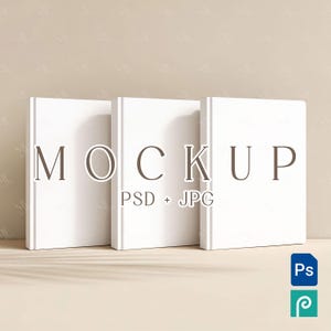 May include: Three white hardcover books standing upright on a light brown surface. The word "MOCKUP" is printed on the front of the books, with "PSD + JPG" below. A blue and green icon is in the bottom right corner.