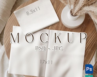 Puede incluir: Una maqueta con dos hojas de papel blancas, una de 21,6 x 27,9 cm y otra de 43,2 x 27,9 cm, con la palabra "MOCKUP" en letras grandes. Un pequeño jarrón blanco con plantas secas se encuentra sobre una superficie de madera.