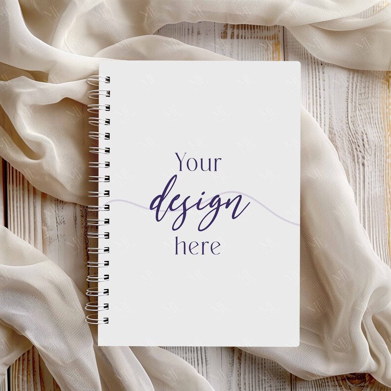 May include: A white spiral bound notebook with the text "Your design here" written in purple on the front cover. The notebook is lying on a white wooden surface with a white sheer fabric draped over it.
