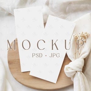 May include: Two blank white rectangular cards on a wooden plate, with the word "MOCKUP" and "PSD + JPG" printed on the image. A white cloth and dried flowers are also in the image.