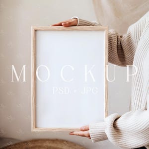 Könnte beinhalten: Eine Person hält eine Poster-Mockup mit hellem Holzrahmen und dem Text "MOCKUP PSD + JPG" unten.
