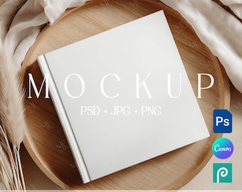 May include: A white square book mockup with the word "MOCKUP" in large white letters. The book is on a wooden tray with a beige cloth and decorative grass. Text on the book says "PSD + JPG + PNG". Icons for Photoshop, Canva, and Photopea are also visible.