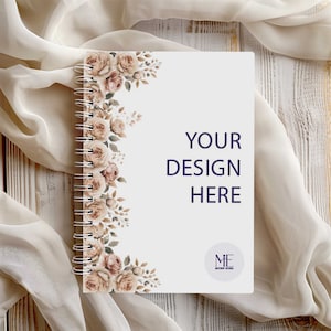 May include: A white spiral bound notebook with a floral design on the left side. The notebook has the text "YOUR DESIGN HERE" in the centre and a logo that says "MF MOCKUP STUDIO" in the bottom right corner.