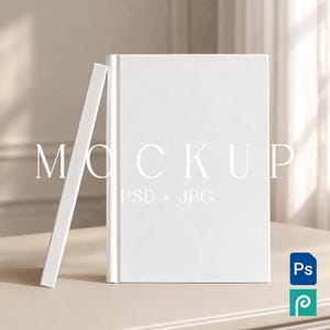 May include: A blank white hardcover book standing upright with a second white book leaning against its side. The text MOCKUP PSD + JPG is overlaid on the front cover. A blue Photoshop icon and a teal icon are visible in the bottom corner.