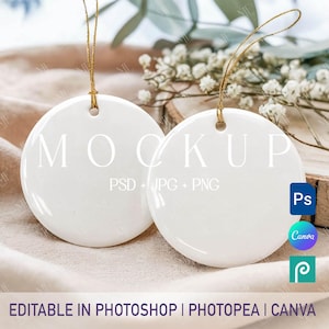 May include: Two white, round ceramic ornaments with gold string hangers. The word "MOCKUP" is printed on the ornaments. The text "PSD + JPG + PNG" is printed below the word "MOCKUP". The text "EDITABLE IN PHOTOSHOP | PHOTOPEA | CANVA" is printed at the bottom.