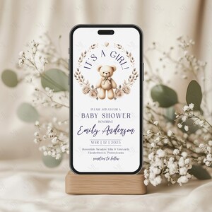 Op de afbeelding: Een digitale uitnodiging voor een babyshower met een illustratie van een teddybeer en een bloemenkrans. De tekst luidt "It's a Girl!" en bevat de naam "Emily Anderson", de datum "Mar 12 | 2025" en de locatie "Rosendale Meadow Villa & Vineyards, Elizabethtown, Pennsylvania".