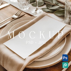 May include: A table setting with a white menu card, plates, silverware, and a beige napkin. The menu card has the word "MOCKUP" printed on it. The setting includes a glass of water and greenery.