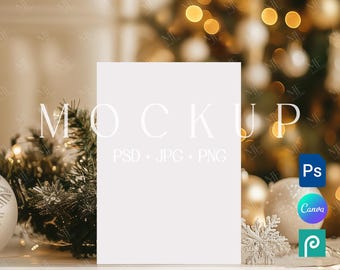 May include: A blank white mockup card with the word "MOCKUP" in a serif font. The card is in front of a blurred background of Christmas decorations, including a Christmas tree, ornaments, and lights. The text "PSD + JPG + PNG" is below the word "MOCKUP".
