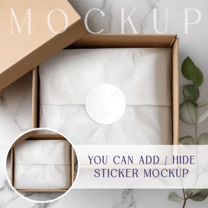 Puede incluir: Una caja de cartón marrón con una pegatina circular blanca en la parte superior. La caja está abierta y llena de papel de seda blanco. El texto "YOU CAN ADD / HIDE STICKER MOCKUP" es visible debajo de la caja.