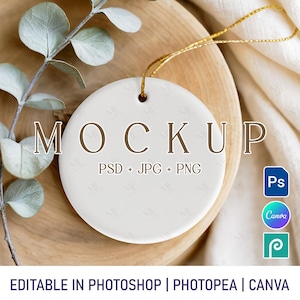 May include: A white, circular ceramic ornament with the word "MOCKUP" in brown lettering. The text "PSD + JPG + PNG" is below. A gold string is attached for hanging. The image also includes the text "EDITABLE IN PHOTOSHOP | PHOTOPEA | CANVA".