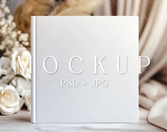 May include: White square book mockup with the text "MOCKUP PSD + JPG" on a white surface with white flowers and a beige fabric background.