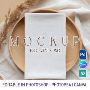 May include: A white folded napkin sits on a wooden plate, with the word "MOCKUP" in large letters. The text "PSD + JPG + PNG" is below the word "MOCKUP". The words "EDITABLE IN PHOTOSHOP | PHOTOPEA | CANVA" are at the bottom.