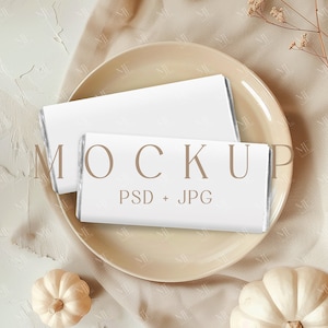 Puede incluir: Dos objetos rectangulares blancos con bordes plateados están sobre un plato beige. El plato está sobre una tela beige, con dos pequeñas calabazas blancas y flores secas. El texto "MOCKUP PSD + JPG" es visible.