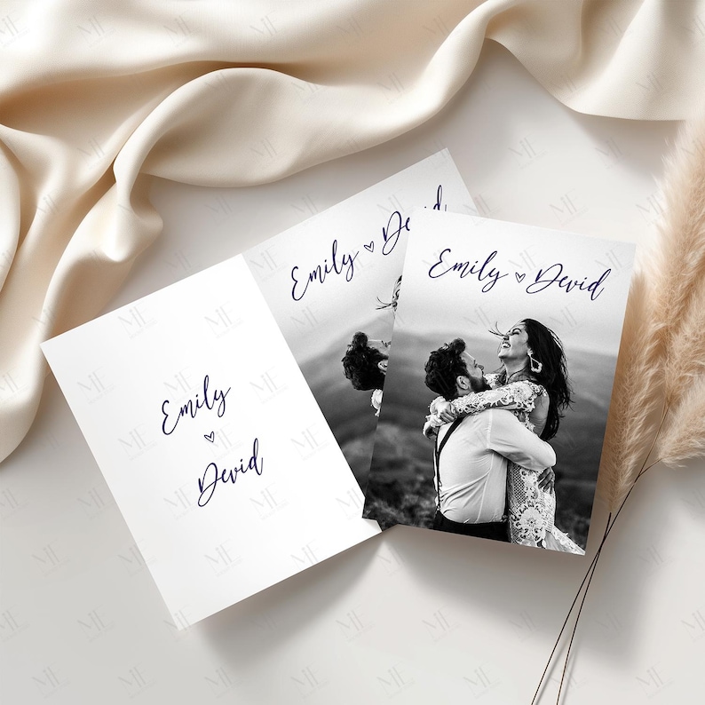 May include: Three white wedding invitation cards with the names "Emily" and "David" in navy blue script. One card features a black and white photo of a couple embracing. The cards are arranged on a white surface.