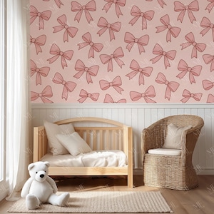 May include: A nursery scene featuring a light pink wall adorned with a repeating pattern of pink bows. A wooden crib, a wicker chair, a white teddy bear, and a beige rug complete the room's decor. The room is bathed in natural light.