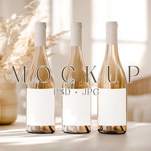 May include: Three clear wine bottles with white labels and white bottle tops are arranged on a light-colored surface. The bottles are filled with a golden liquid. The word "MOCKUP" is printed in a serif font above the bottles. The text "PSD + JPG" is printed below the bottles.