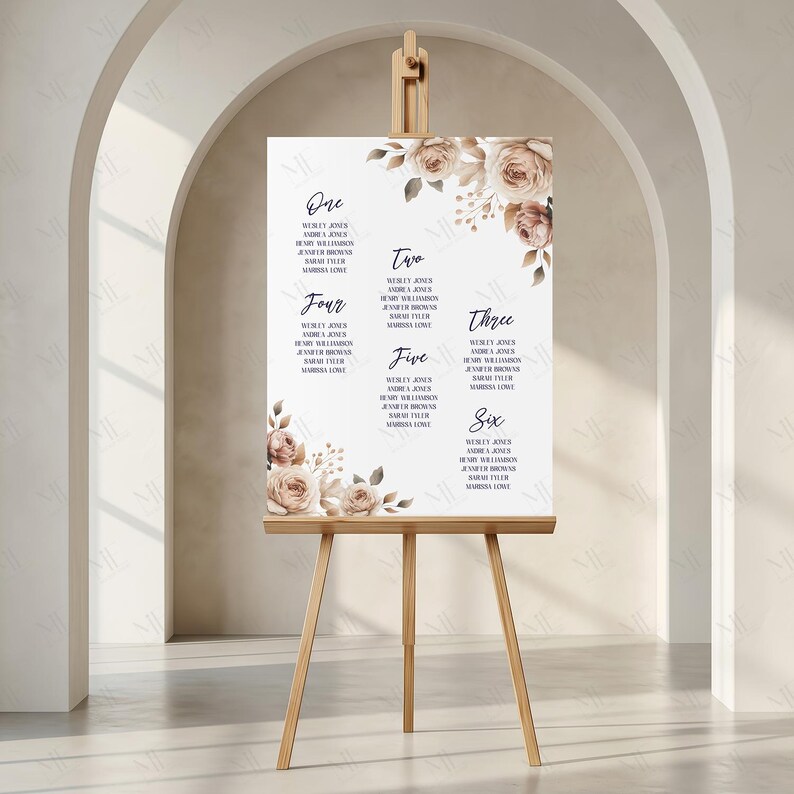 May include: A wedding seating plan displayed on a wooden easel. The white sign has names arranged by table number, with brown and beige floral decorations. The numbers are written in a decorative font.