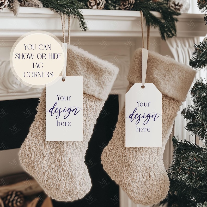 May include: Two beige Christmas stockings with white tags that read "Your design here." The stockings are hanging from a white mantelpiece decorated with pine needles and pine cones. The text "YOU CAN SHOW OR HIDE TAG CORNERS" is in a circle.