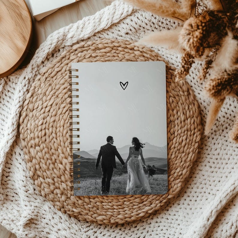 May include: A gray spiral bound notebook with a black heart on the front cover. The notebook has a black and white photo of a couple walking away from the camera on a hilltop.