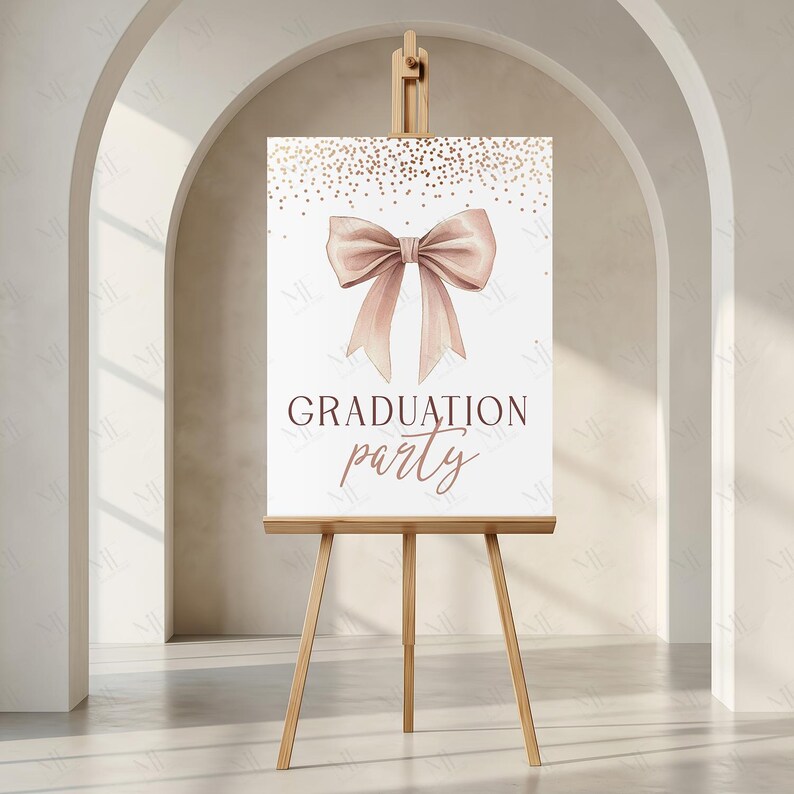 May include: A graduation party sign displayed on a wooden easel. The white sign features a blush-coloured bow and gold confetti. The words "GRADUATION party" are written in a dark brown script font, suitable for a celebration.