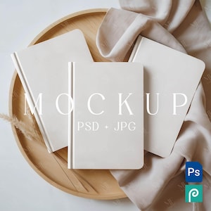 May include: Three off-white hardcover notebooks arranged on a light wooden tray with a beige fabric and dried plant accents. The word "MOCKUP" is displayed across the notebooks, with "PSD + JPG" below. A Photoshop and a Procreate icon are in the bottom right corner.