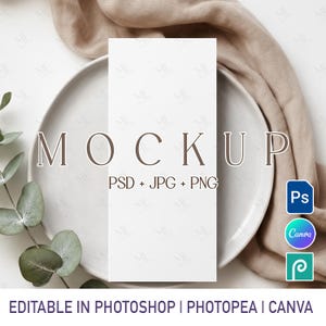 May include: A white rectangular mockup card on a white plate, with a beige cloth draped behind it. The word "MOCKUP" is displayed in brown letters. Text below reads "PSD + JPG + PNG". Icons for Photoshop, Canva, and Photopea are visible. The text "EDITABLE IN PHOTOSHOP | PHOTOPEA | CANVA" is at the bottom.