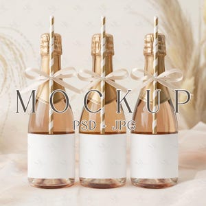 May include: Three champagne bottles with gold foil tops, white labels, and gold and white striped straws. Each bottle is adorned with a cream-colored ribbon. The word "MOCKUP" is printed in the image.