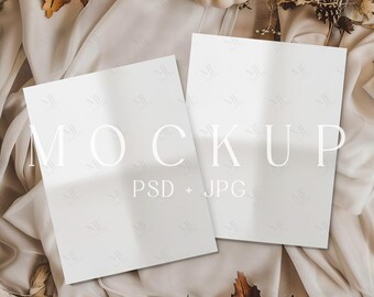 Puede incluir: Dos maquetas rectangulares blancas con la palabra "MOCKUP" en fuente grande y elegante. El texto "PSD + JPG" está debajo. Las maquetas están sobre un fondo de tela beige con calabazas y follaje de otoño.