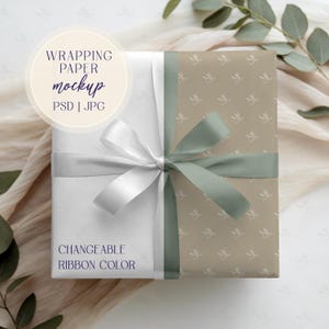 Puede incluir: Un regalo envuelto con papel de regalo blanco y beige, atado con una cinta blanca y verde salvia. El papel de regalo tiene un patrón repetido de las letras "ME". El texto de la imagen dice "WRAPPING PAPER mockup PSD | JPG CHANGEABLE RIBBON COLOR".