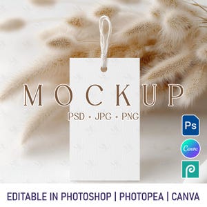 Puede incluir: Maqueta de etiqueta rectangular blanca con una cuerda marrón atada. La etiqueta está sobre una superficie blanca con hierba beige seca en el fondo. El texto "MOCKUP" está impreso en marrón en la etiqueta, junto con el texto "PSD + JPG + PNG".