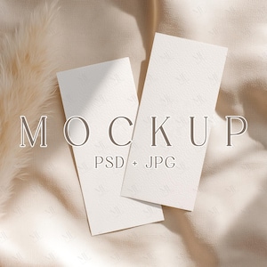 May include: Two off-white rectangular cards with a textured surface, slightly overlapping, against a beige fabric background. The word "MOCKUP" is at the top, with "PSD + JPG" below it.