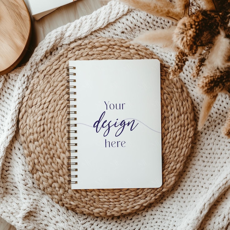 May include: A white spiral bound notebook with the text "Your design here" on a woven straw mat and a white knitted blanket.